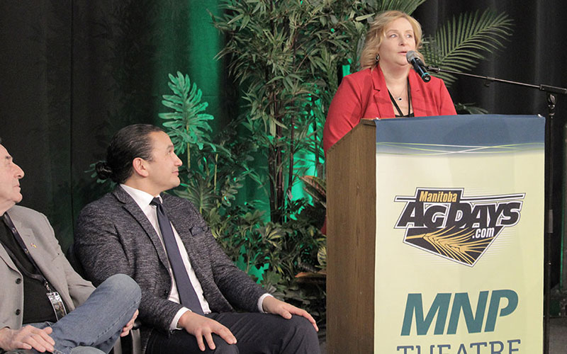New Keystone Centre CEO and General Manager, Connie Lawrence, addresses the audience at Ag Days 2024, while Manitoba Premier Wab Kinew watches from the stage.